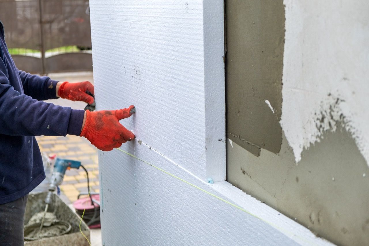 Construction worker installing styrofoam insulation sheets on house facade wall for thermal protection. Servicios de Eizalar